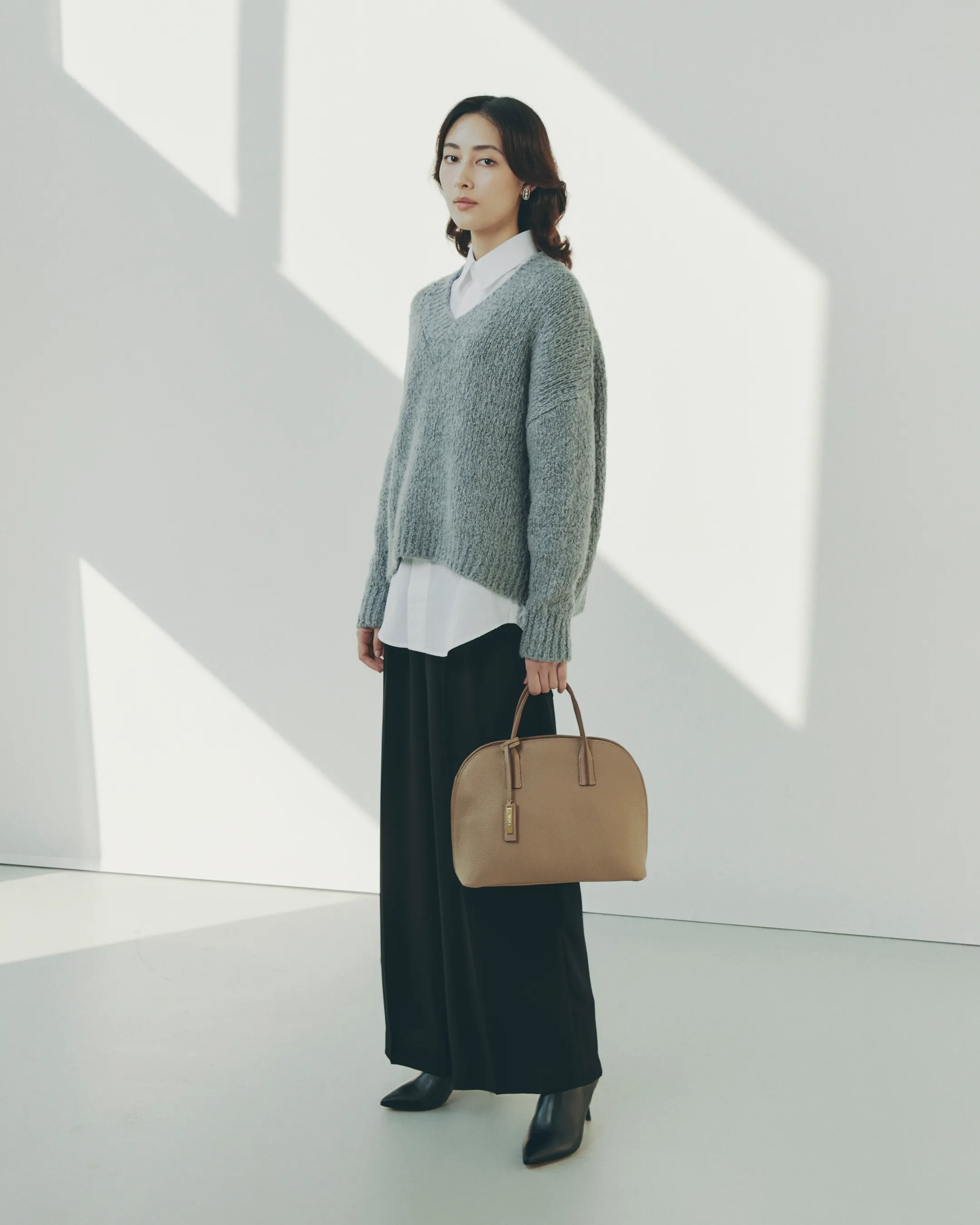 スカリオーネ Vネック プルオーバーをブリエンヌ・パリ・ディス シャツに重ねて着用しているモデルがWAKO×MAURO GOVERNA ハンドバッグを持つ姿を斜めから捉えた様子