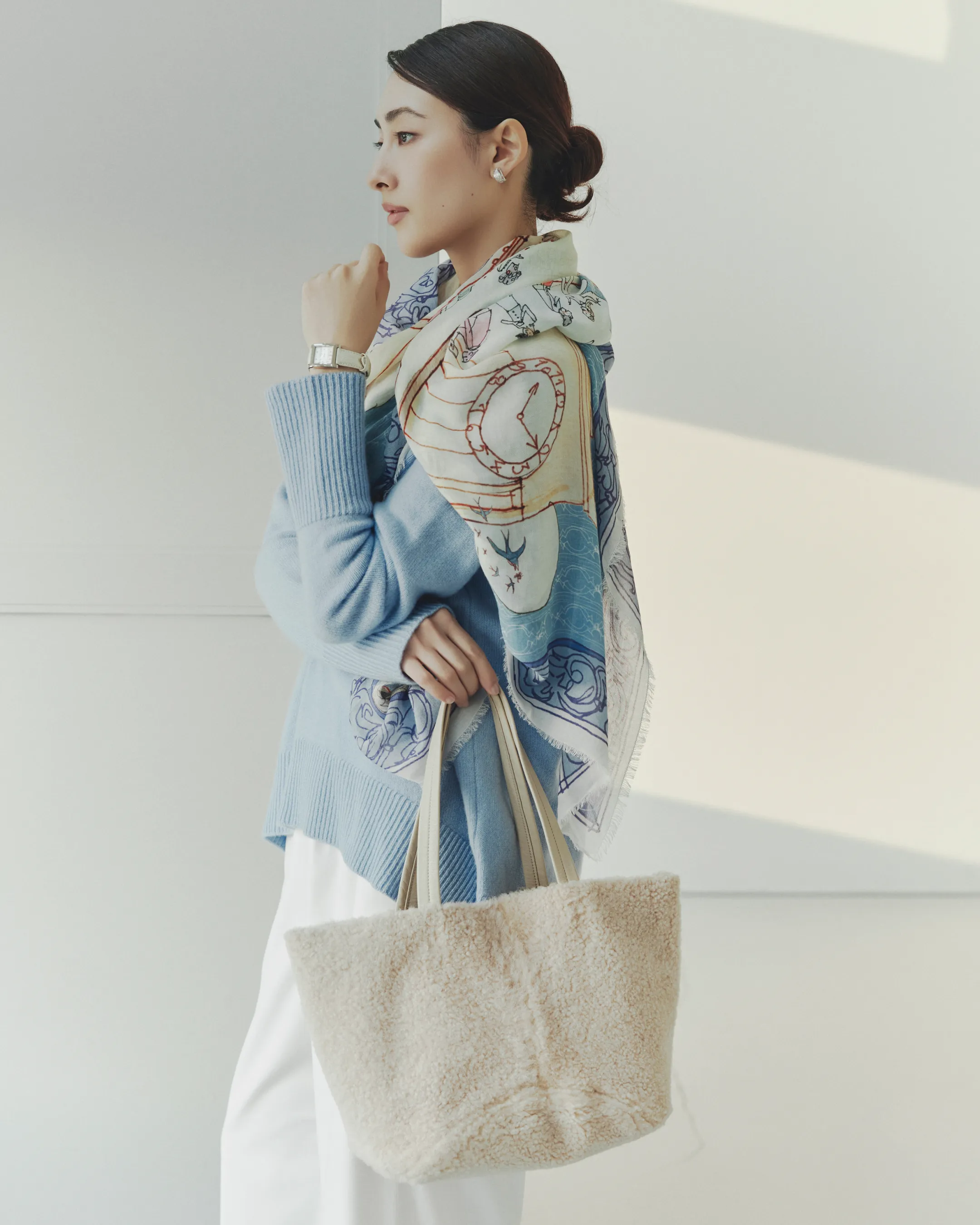 スカリオーネ プルオーバーを着用し、ファリエロ サルティ ストールを肩にかけているモデルがMANACO トートバッグスモール ムートンを持ち綺麗な姿勢で立っている様子
